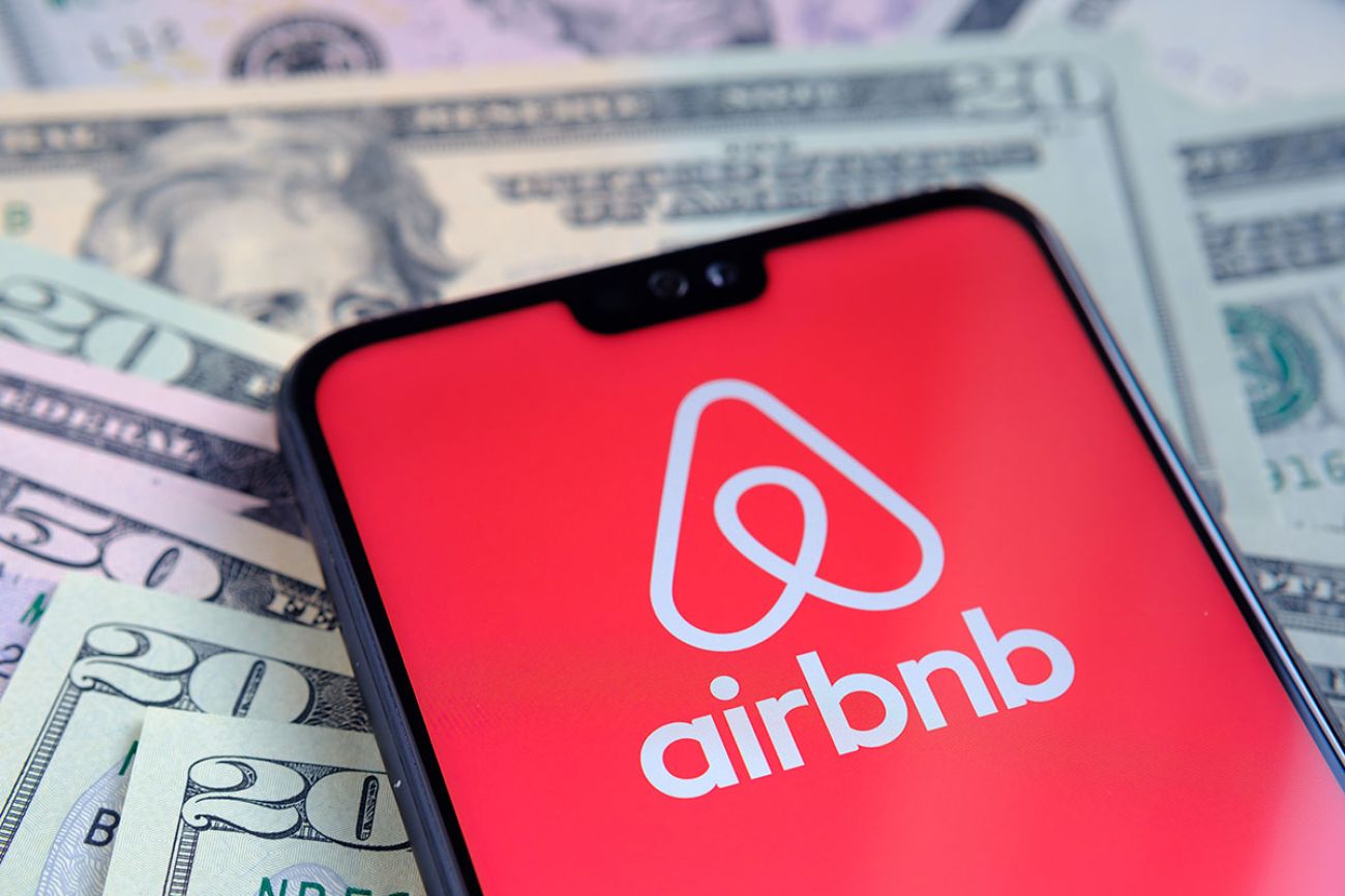 Airbnb app logo seen on the screen of smartphone, placed on dollar bills.