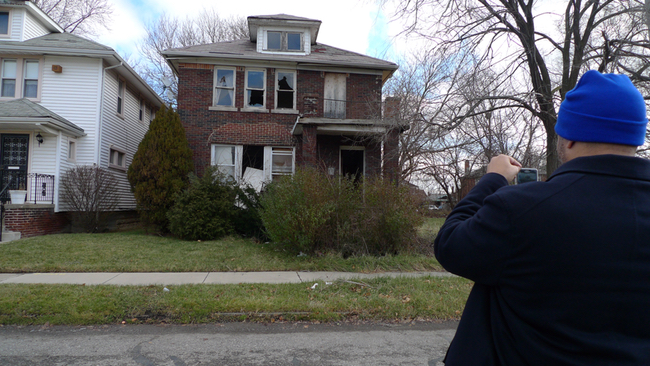 Marshall Bullock photographs a blighted house scheduled to be boarded up in Detroit’s 7th Council District, where he serves as district manager. Before-and-after photos of such projects are part of his weekly reports to the city’s Department of Neighborhoods. (Bridge photo by Nancy Derringer)