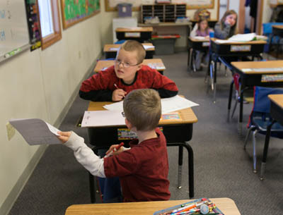 In a classroom teaching kindergarteners to 8th graders, older students are called on to help younger kids with lessons. At the Eccles Schools, Ian Morley, top, in 4th grade, helps kindergartner Conner Woodchisky check his classwork (Bridge photo by Brian Widdis)