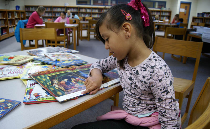 Lakeshore first grader Leslie Trujillo reads while awaiting her turn at DIBELS testing, a measure of her reading ability. She lives with her family in a complex at a migrant worker camp near Holland. When winter comes, she and her family will move to Mexico. (Bridge photo by Pat Shellenbarger) 