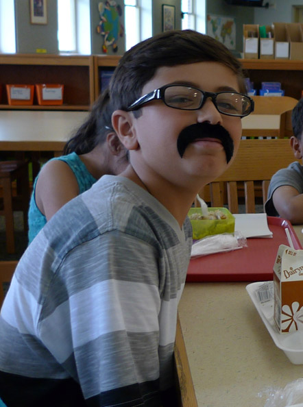 Geer Park Elementary fifth-grade student Amen Salha proudly shows off the mustache he was awarded for academic achievement in social studies; the prize included the right to wear it in school all day. (photo by Nancy Derringer)
