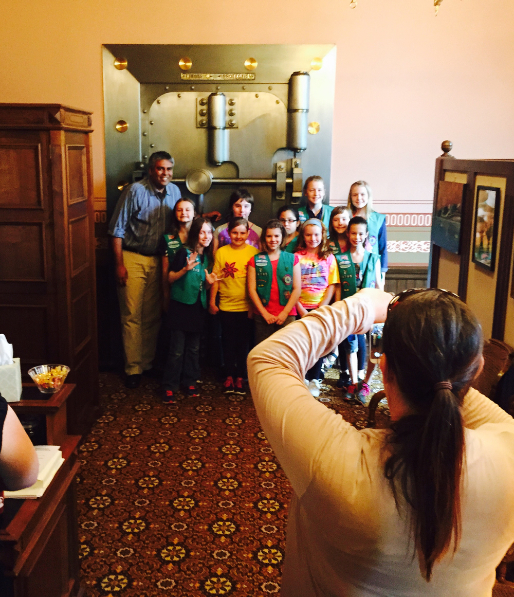 Sam Singh poses for a photo with a visiting Girl Scout troop in his Lansing office. The floor leader’s office was once that of the state treasurer, hence the vault, a popular photo location. (Bridge photos by Nancy Derringer) 