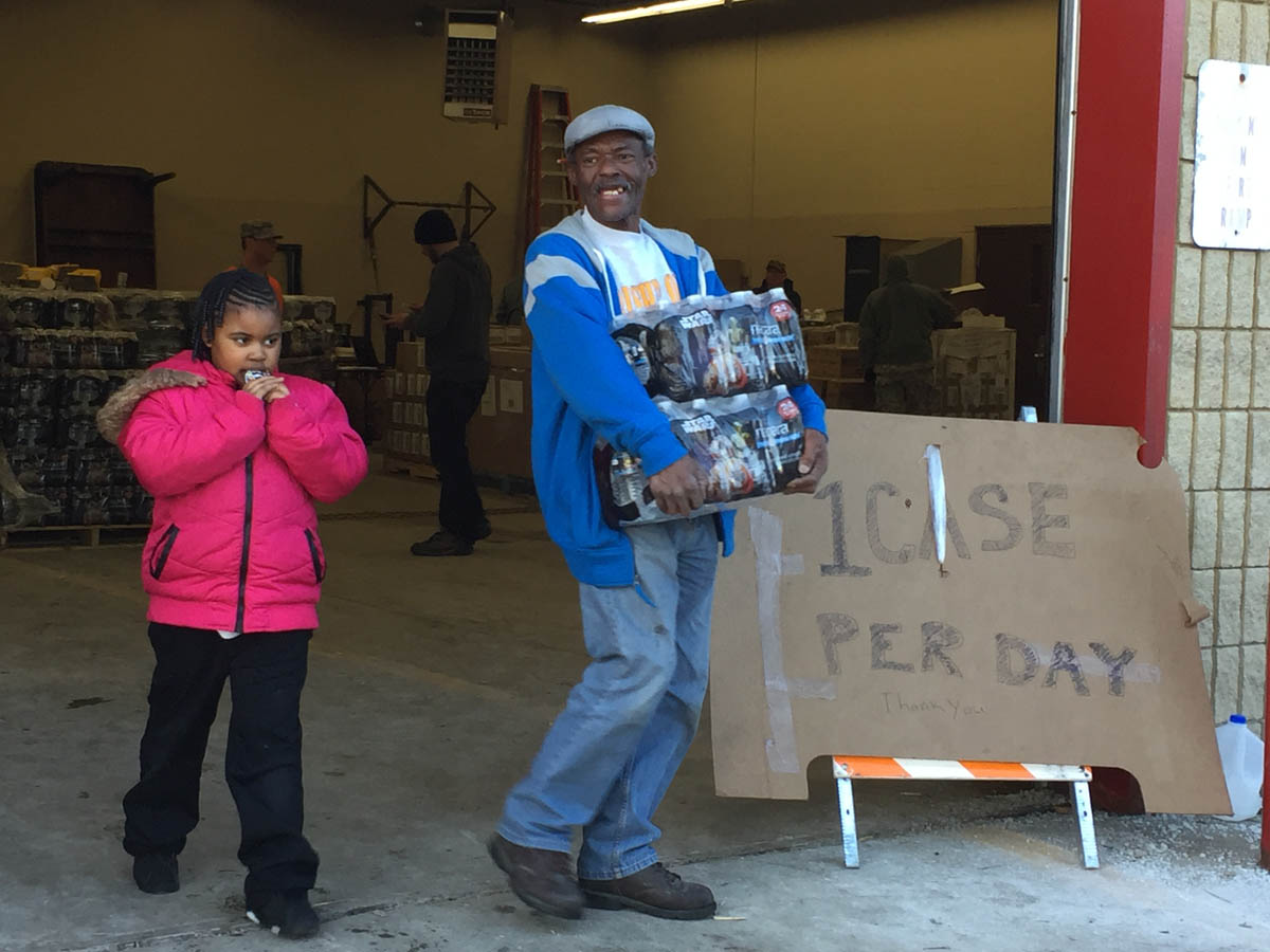 Curtis West, 57, and his daughter, Brooklyn Pratcher, 7, get two cases of free bottled water at a fire station. (Bridge photo by Chastity Pratt Dawsey)
