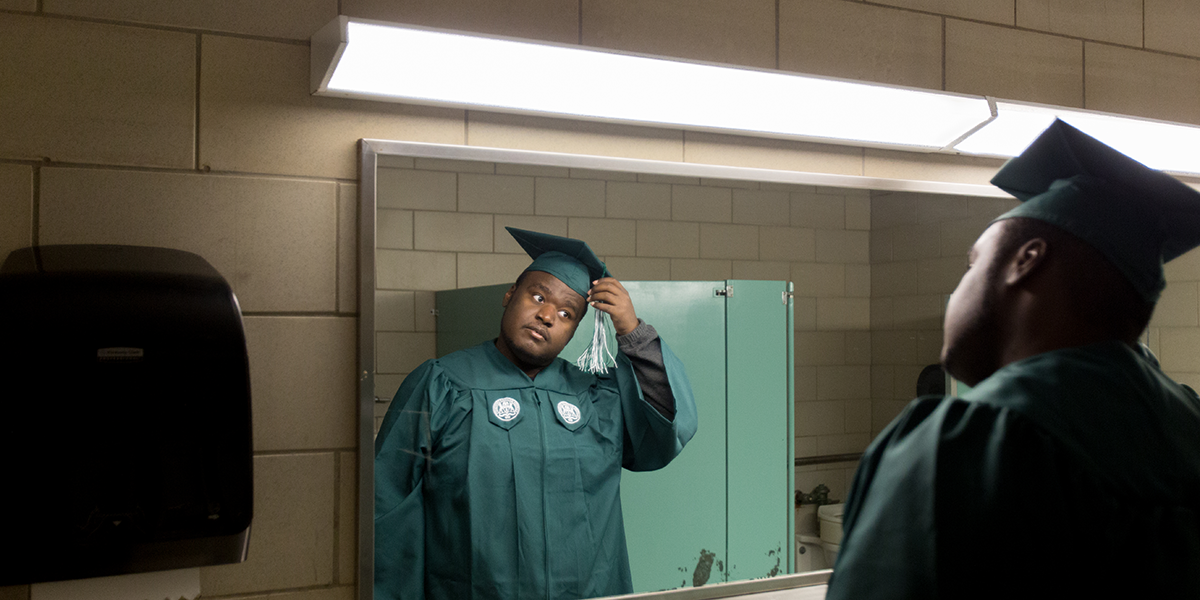Ramone Williams puts on his cap and gown in the locker room at Eastern Michigan University’s rec building before his graduation. When Williams was homeless, he kept personal items in this locker room. (Bridge photo by Brian Widdis)