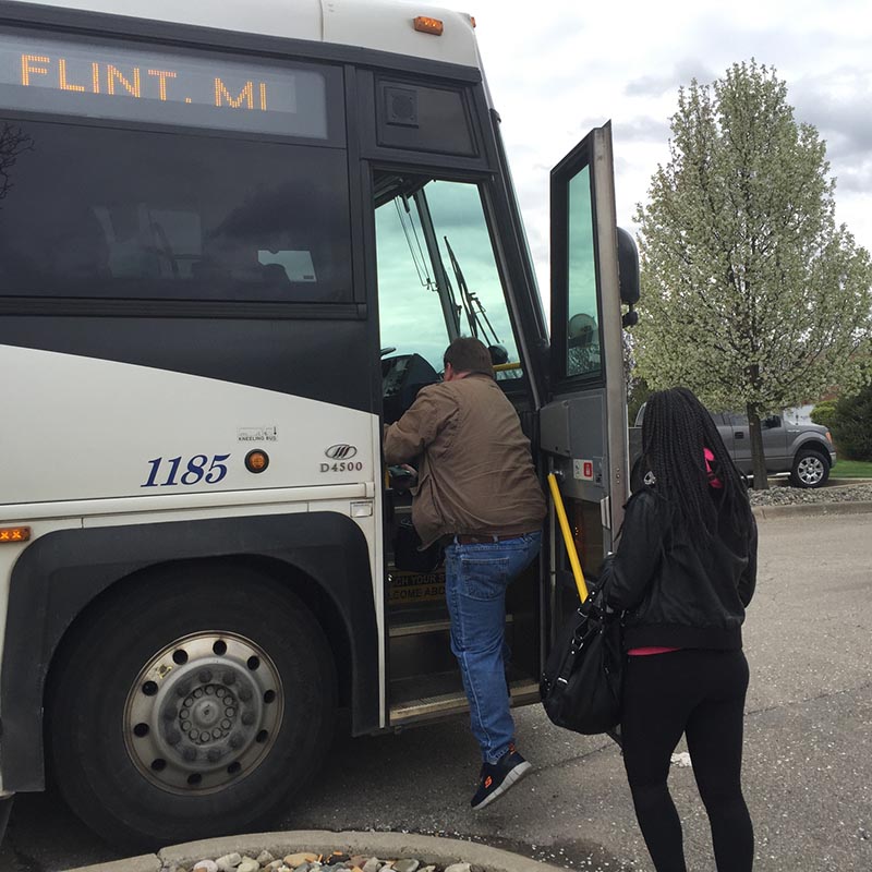 Workers board a bus leaving Tribar Manufacturing in Howell headed home to Flint in April (Bridge photo by Chastity Pratt Dawsey)
