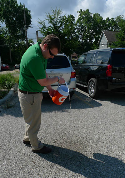 Michael Staal, civil engineer for the city of Grand Rapids, demonstrates the porous pavement at Joe Taylor Memorial Park. The cooler full of water he poured out didn’t run to a gutter or puddle; rather, it seeped through the surface of the lot and into an underground infiltration basin, where it will eventually go back into the soil. (Bridge photo by Nancy Derringer) 