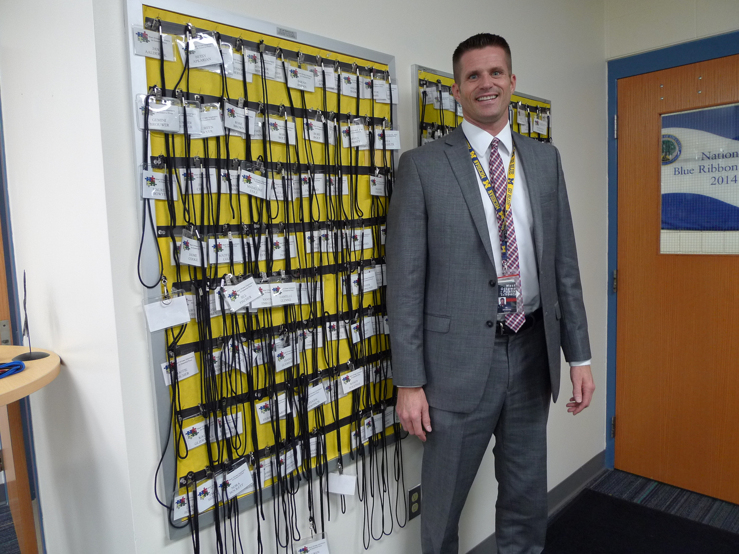 Jens Milobinski, principal at Lakeshore Elementary, stands in front of the dozens of lanyards worn by the parent volunteers he recruits to read one-on-one with students during the school day. (Bridge photo by Nancy Derringer)