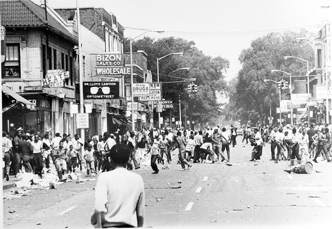 People on 12th Street on Sunday, July 23, 1967, several hours after the raid on the blind pig, which was located in the building in the left background, with the “Economy Printing” sign. (Detroit Free Press photo.)