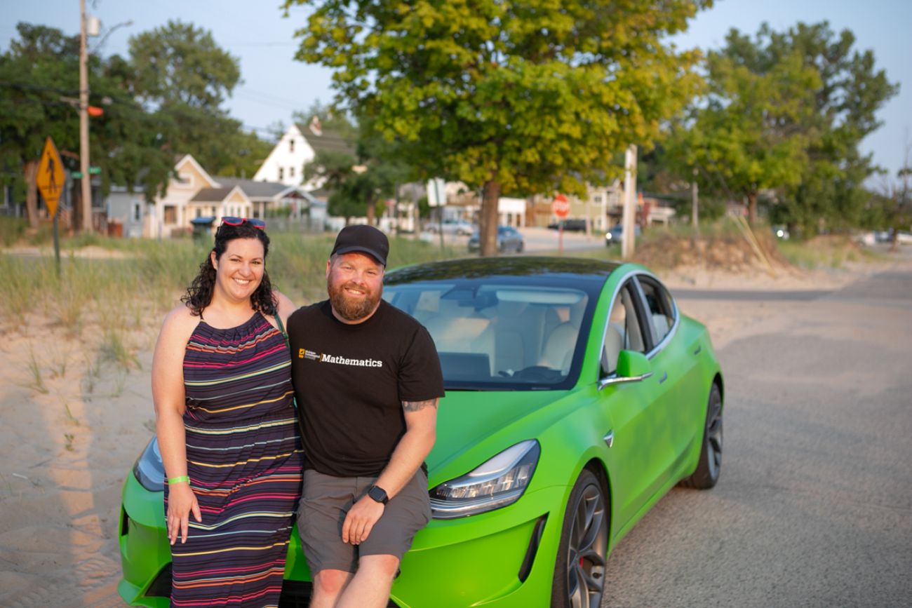 A couple posing in front of a green EV car
