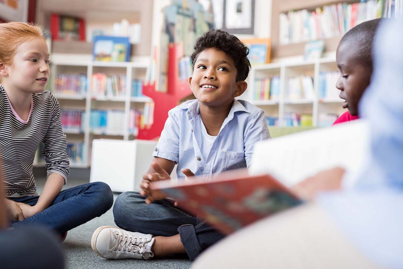 group of kids sitting on floor in circle around the teacher and listening a story.