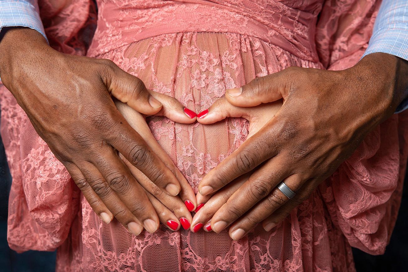 Hands of young African American black couple forming a heart shape on the pregnant belly of the woman with man's hands on top 