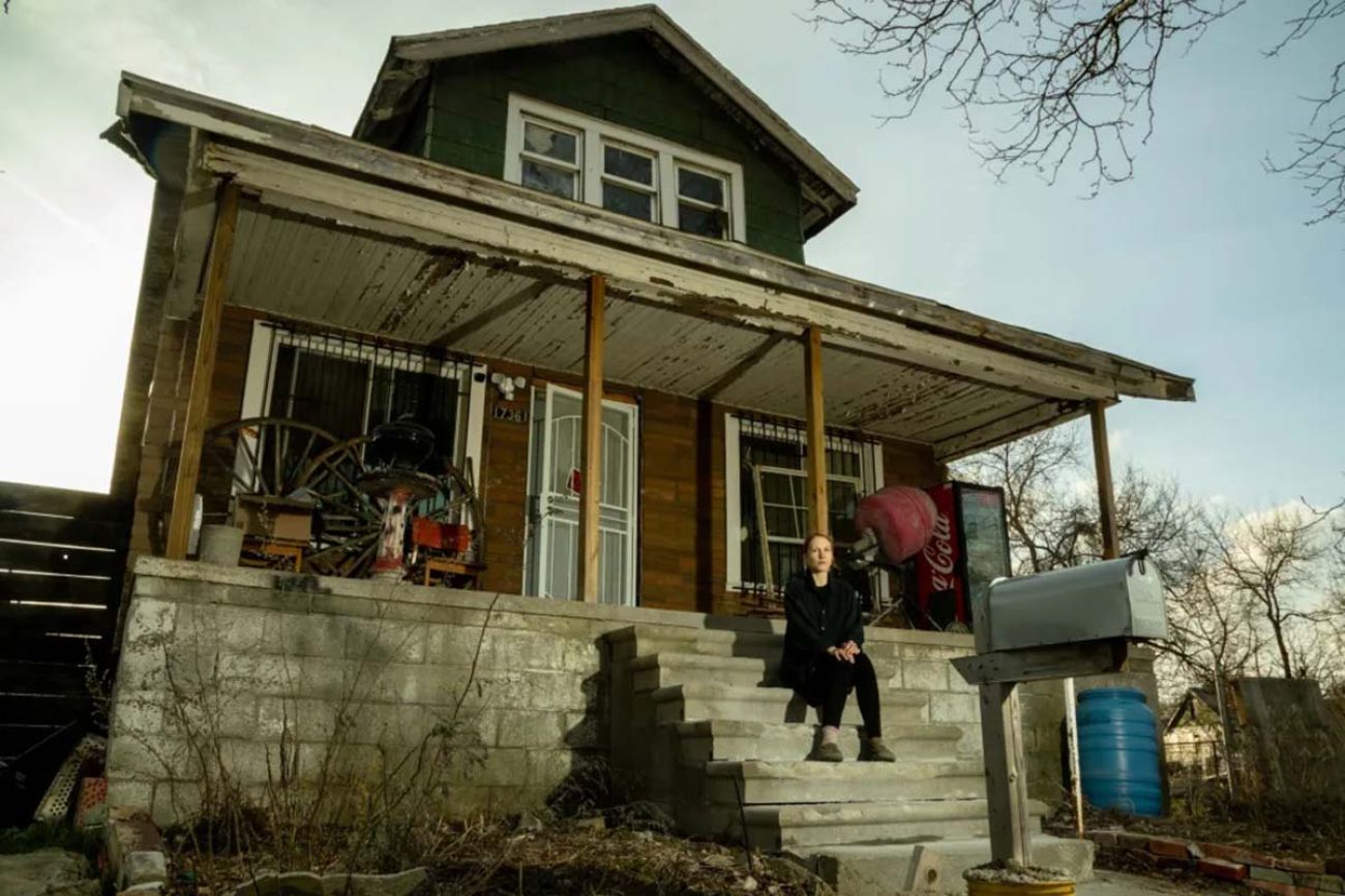 A woman sitting on steps of a porch of a brown house.