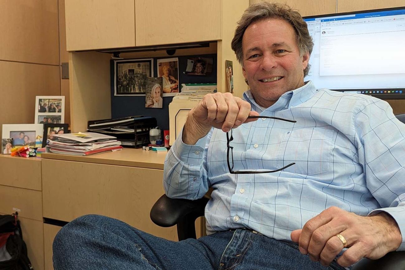 Man sitting in a chair in an office. On his desk are photos of loved ones.