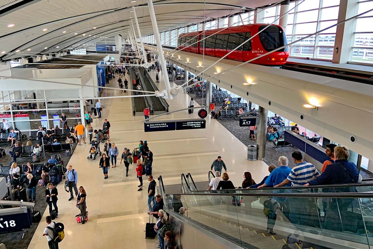 The busy passenger terminal at the airport in Detroit. Lots of people walking, a red tram 