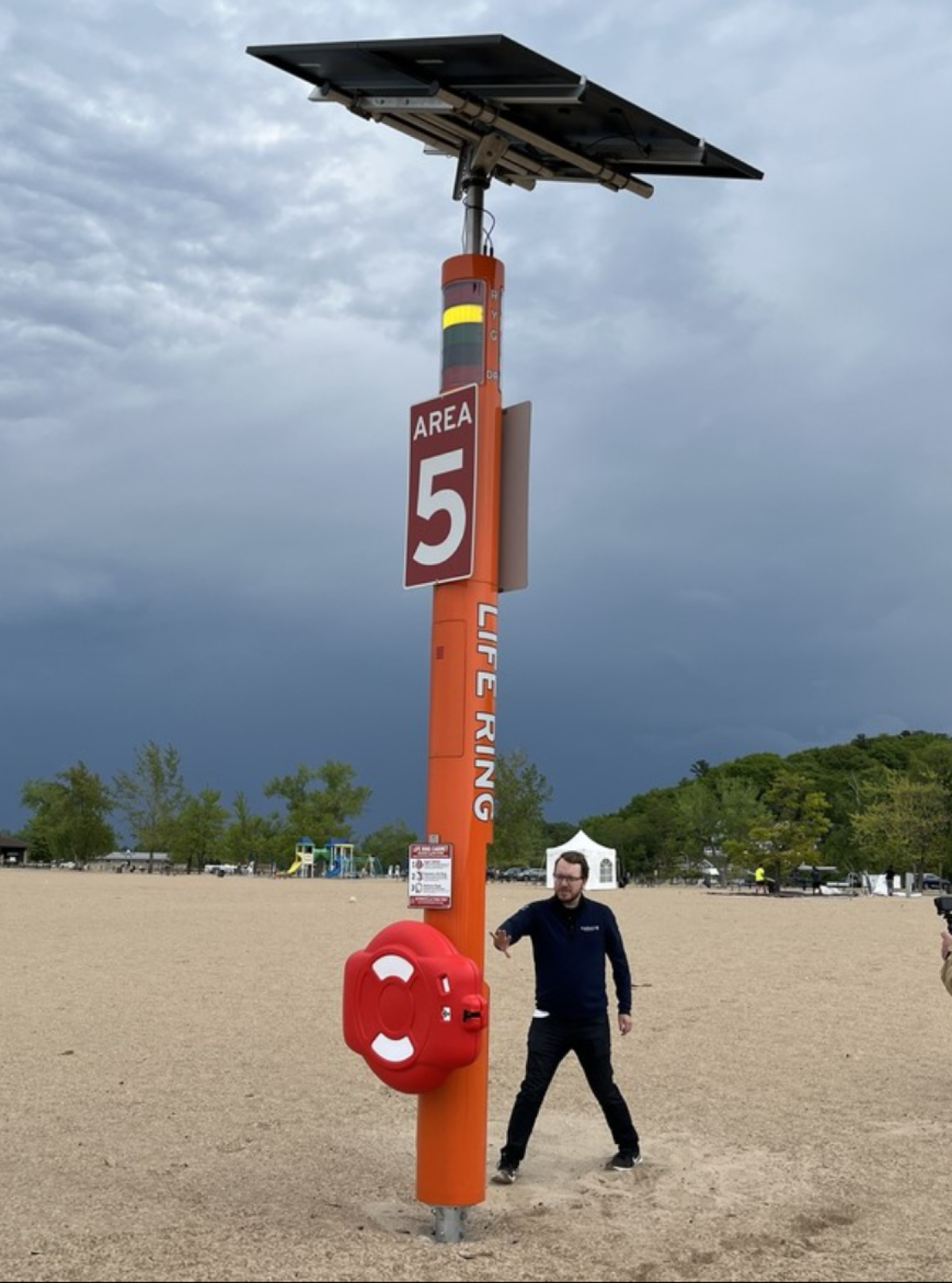 An orange pole on the beach. A man is standing by it