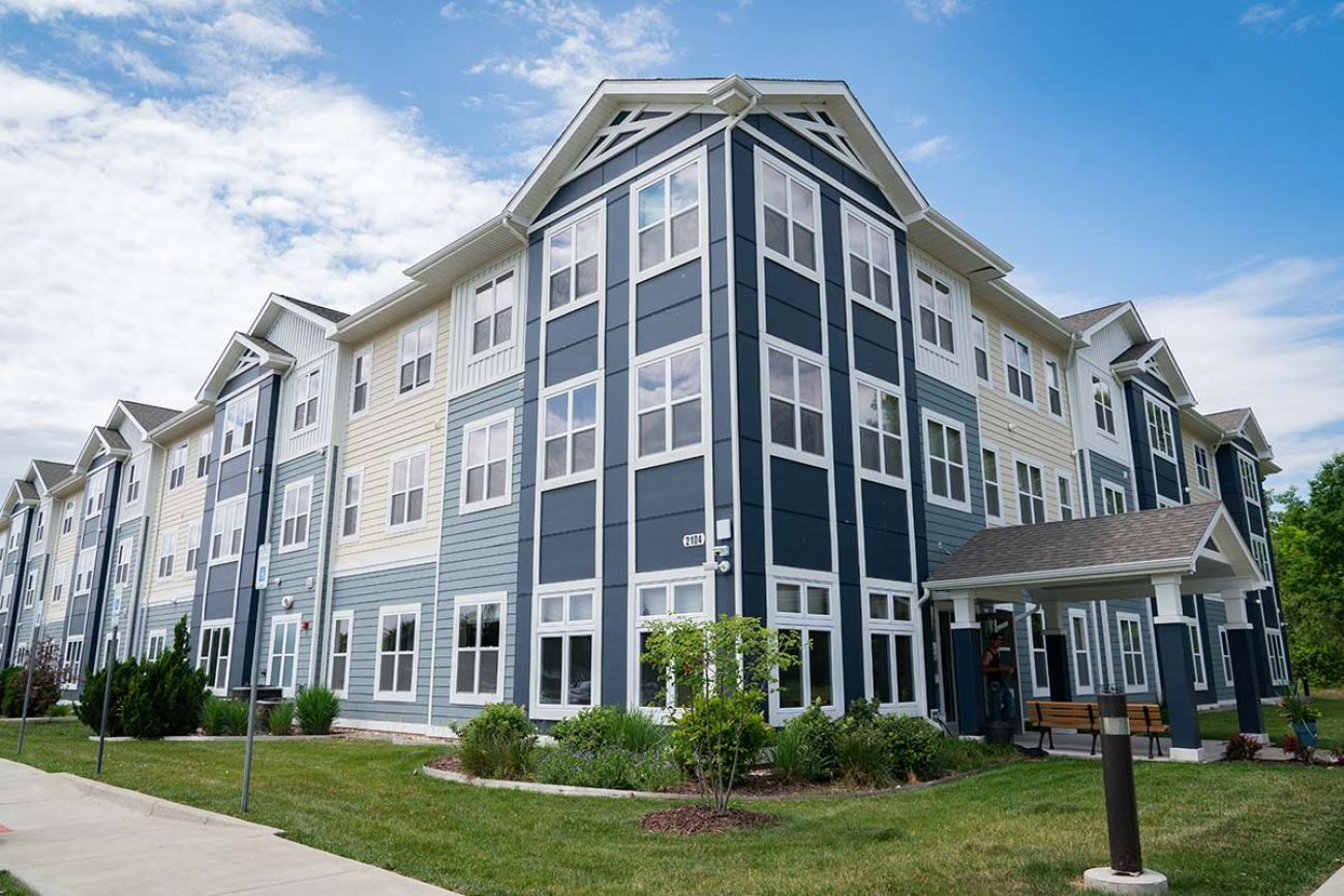 A wide, three-story building. It has blue and white siding 