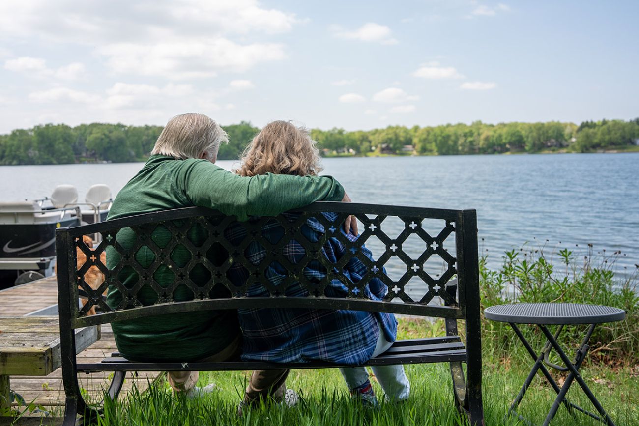 two people sitting on a bench, looking at a lake