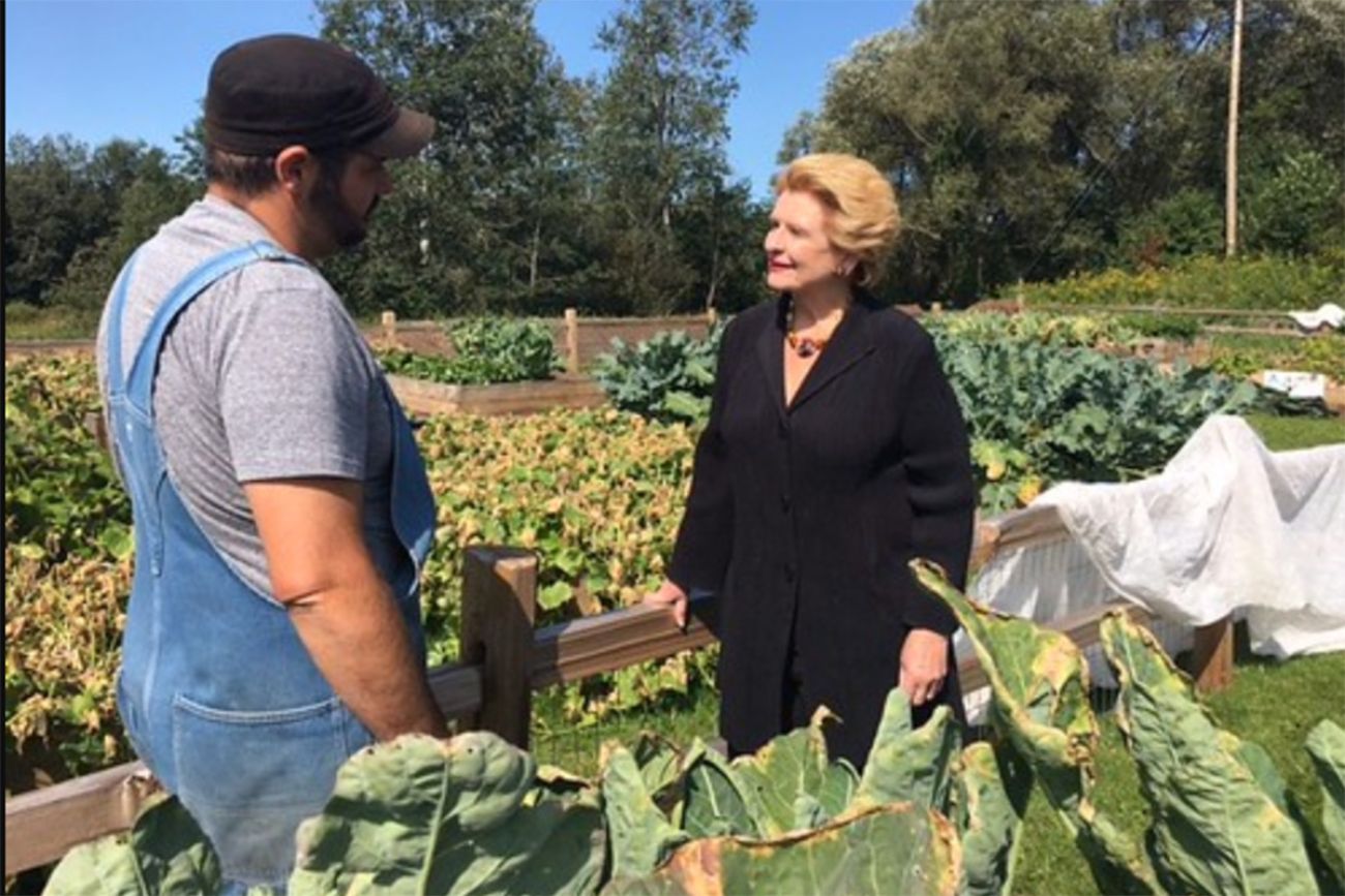 Debbie Stabenow is standing in a farm field. She is talking to a man in overalls 