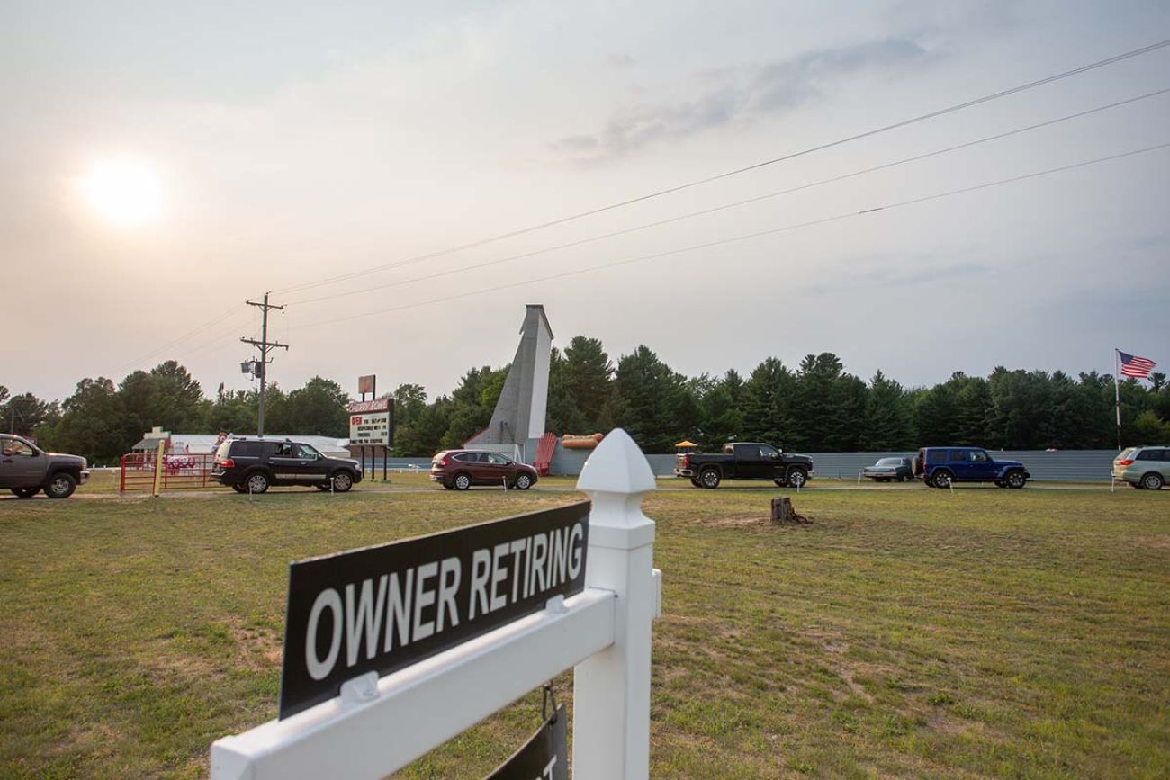 A sign stating the owner is retiring in the foreground. Cars lining up to go in the background