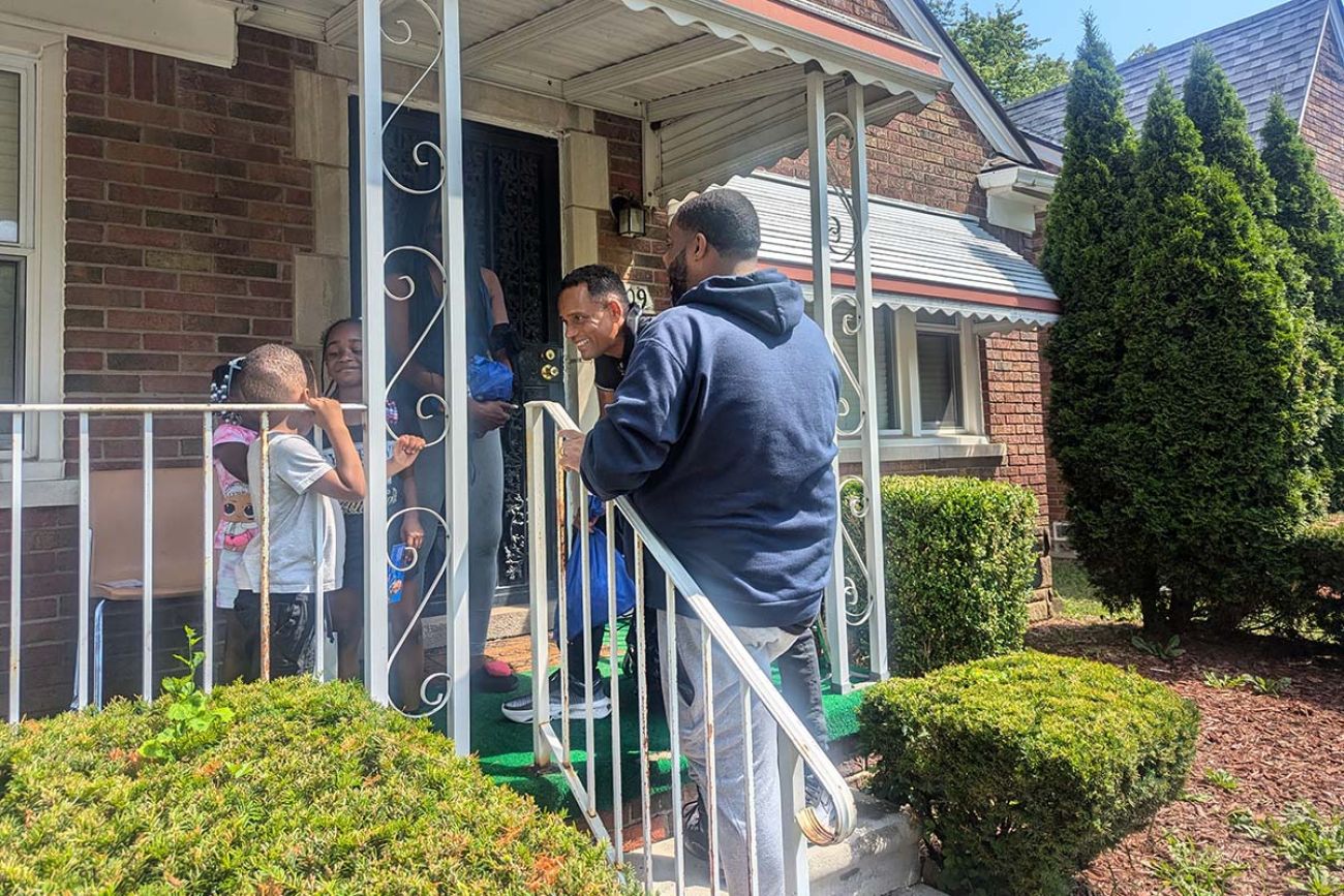 Hill Harper and state Rep. Donavan McKinney are standing in the front porch of the house, talking to a family