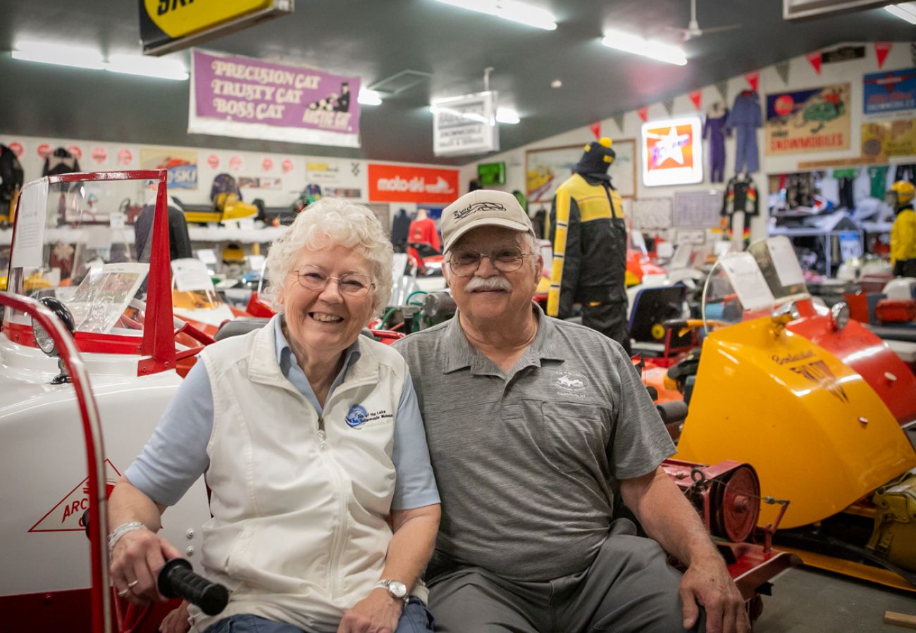 Two people sitting in a snow mobile museum 