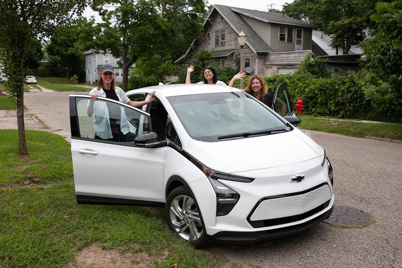 Bridge Michigan journalists Paula Gardner, Kelly House and Asha Lewis pose for a picture around a white EV