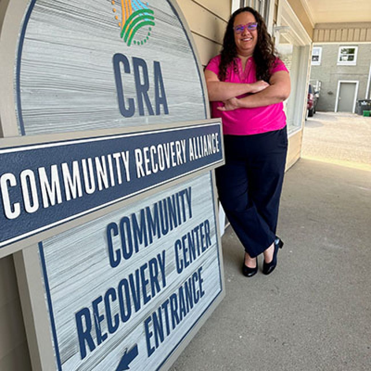 Kaitlin Koucky posing photo, next to a sign for the Community Recovery Alliance in Petoskey