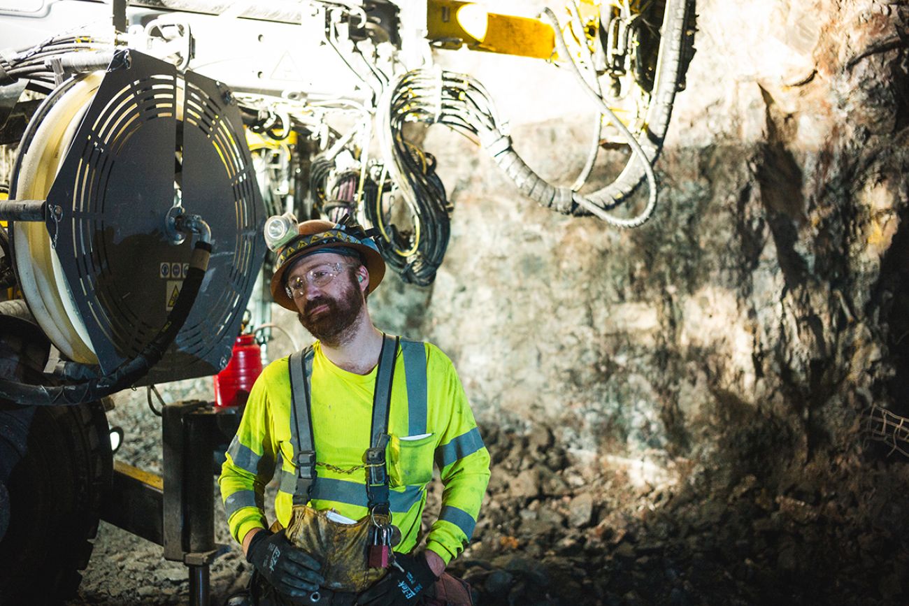 Paul Johnson, wearing a bright green shirt and hard hat, stands next to a piece of machinery inside the Eagle Mine in Michigan