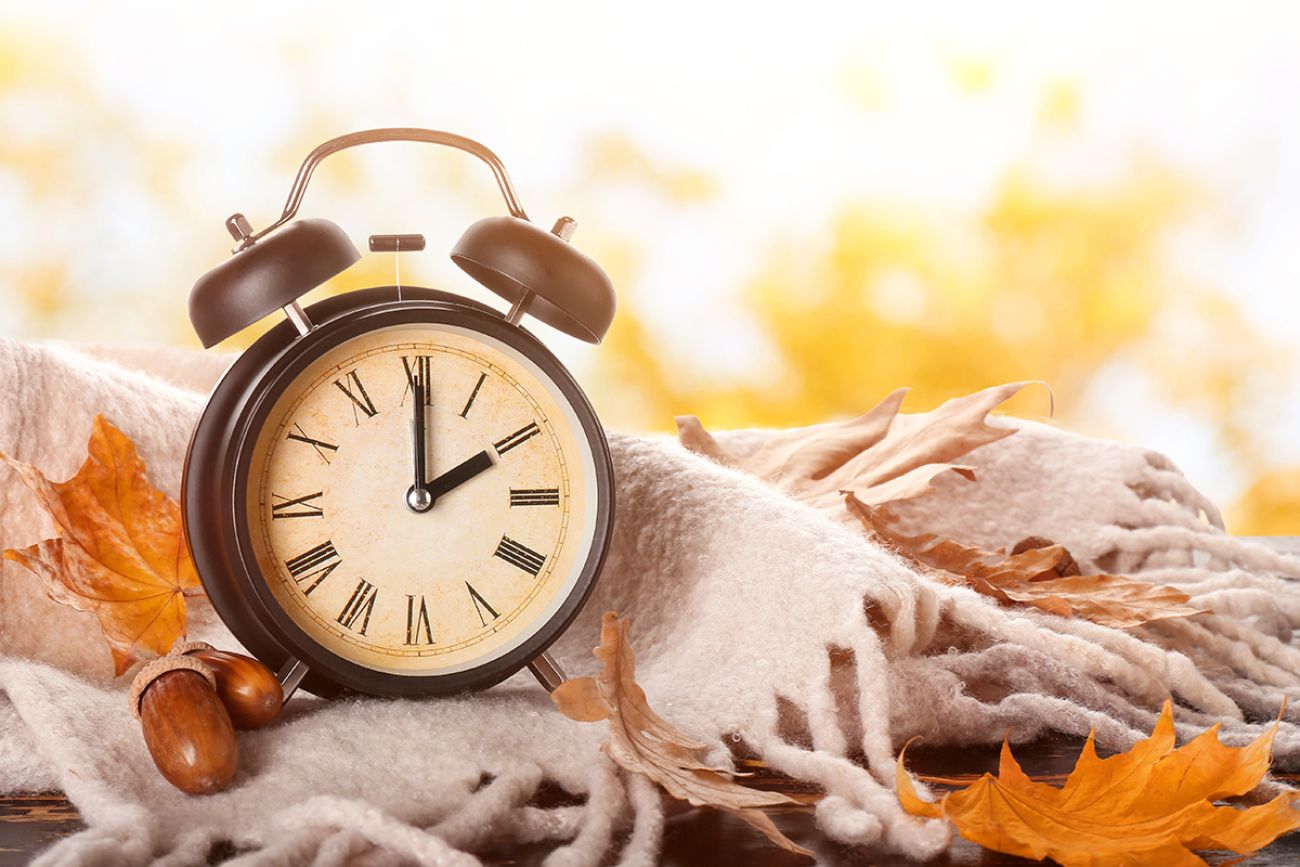 Alarm clock, acorns, scarf and autumn leaves on table outdoors