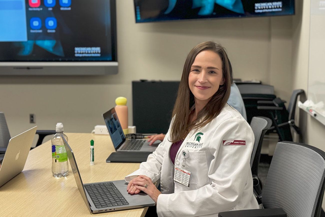 Bethany Russell, wearing a white doctor's coat, sits a table