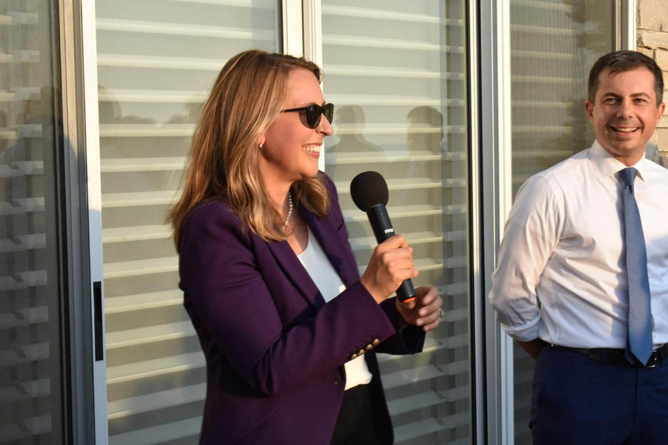 U.S. Rep. Hillary Scholten speaks into a microphone. Pete Buttigieg stands next to her