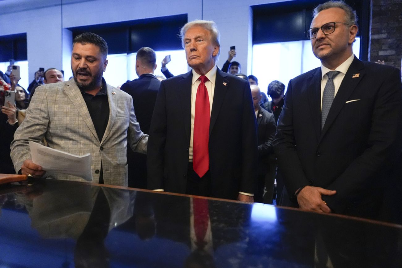 Donald Trump, wearing a dark colored suit and a red tie, stands next to Albert Abbas and Massad Boulos