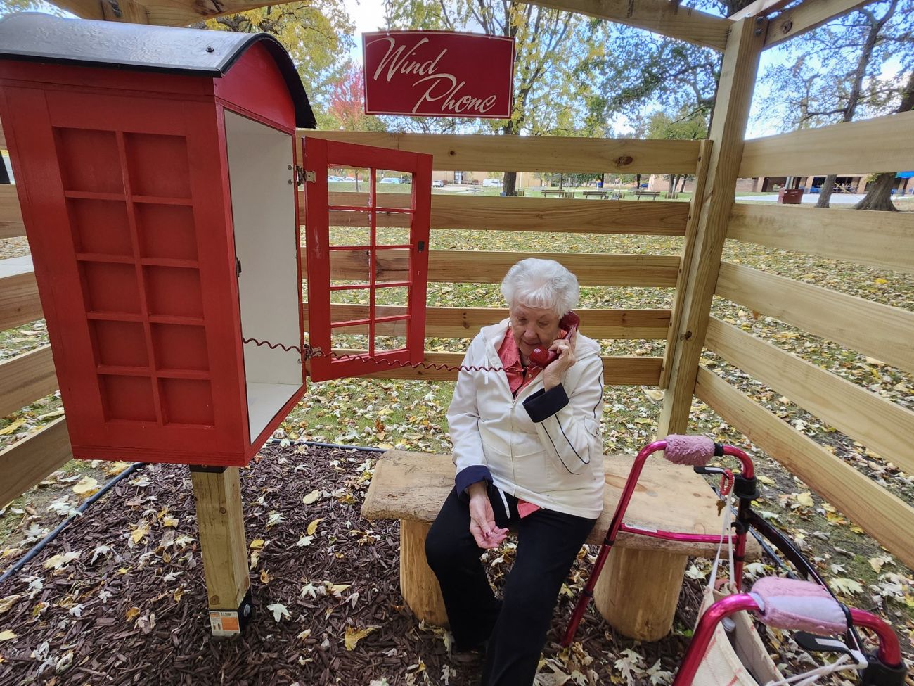 Shirley Franchock sits on a bench. She is speaking into a wind phone in a red box