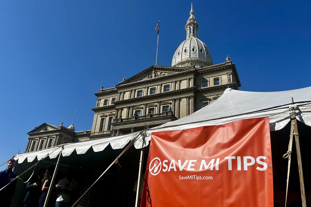 A red sign that says "Save MI Tips" in front of the Michigan Capitol Building
