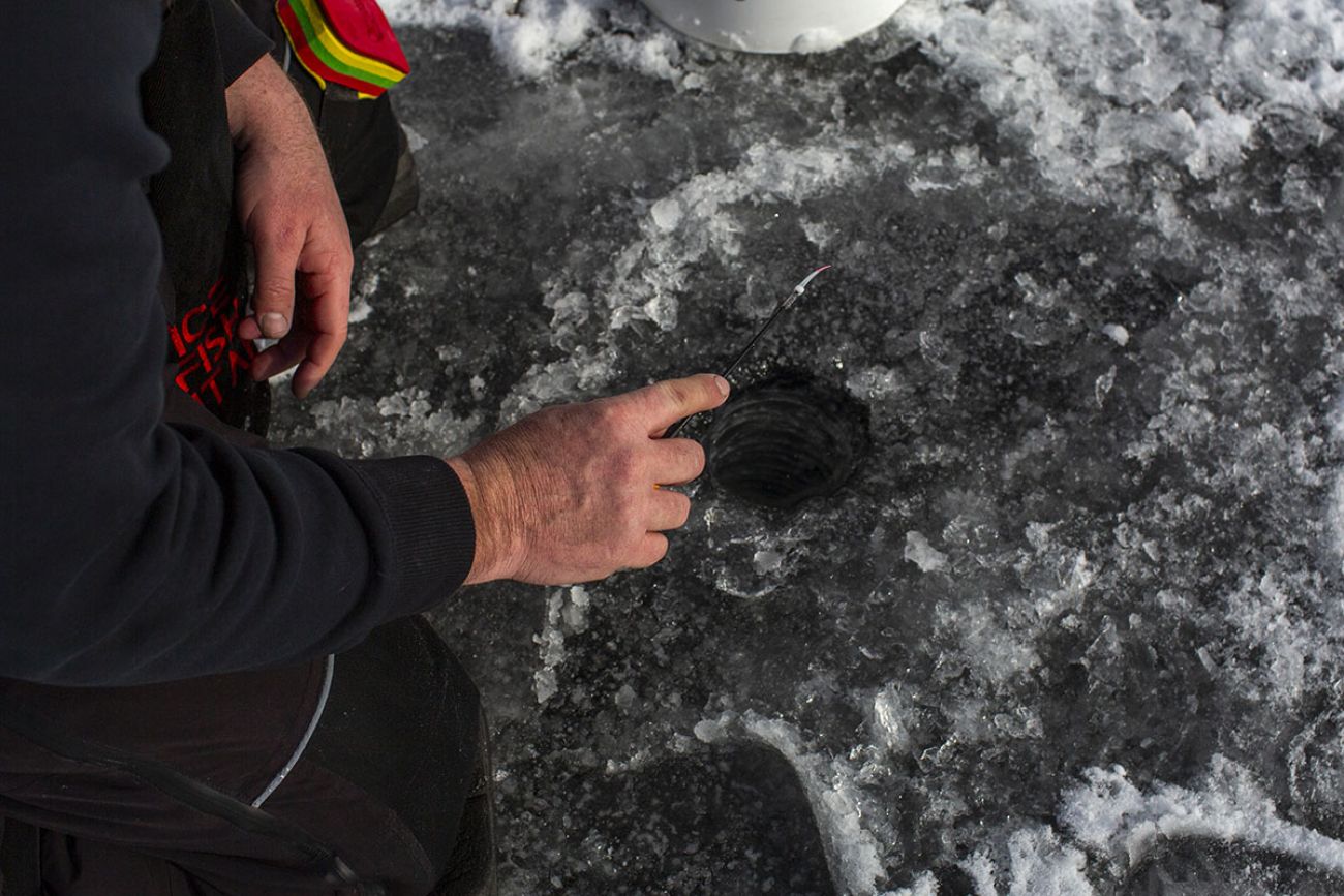 Joe Martinez kneeling by a hole in the ice. 