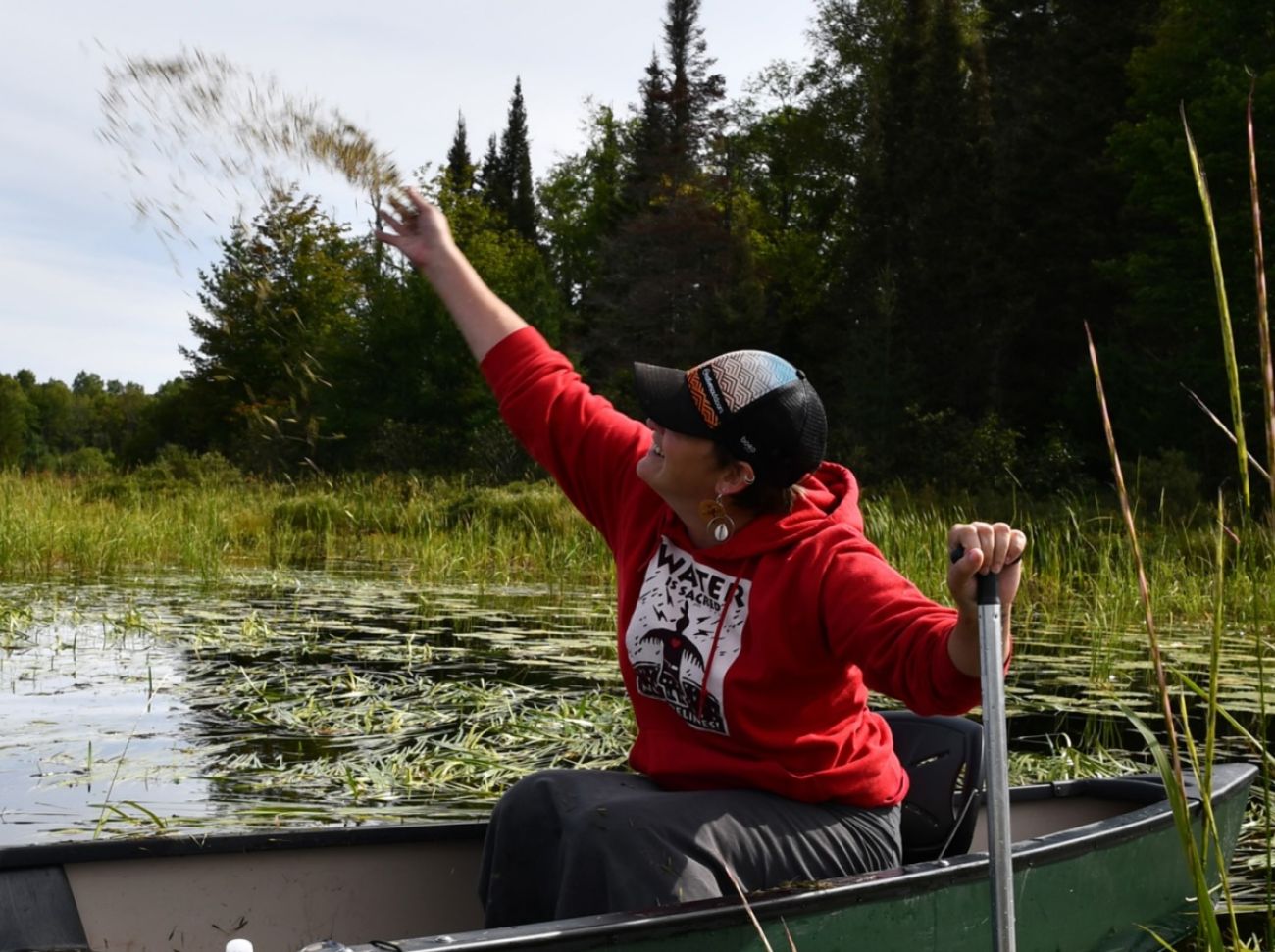 Cortney Collia is sitting in a boat. She is throwing seeds. 