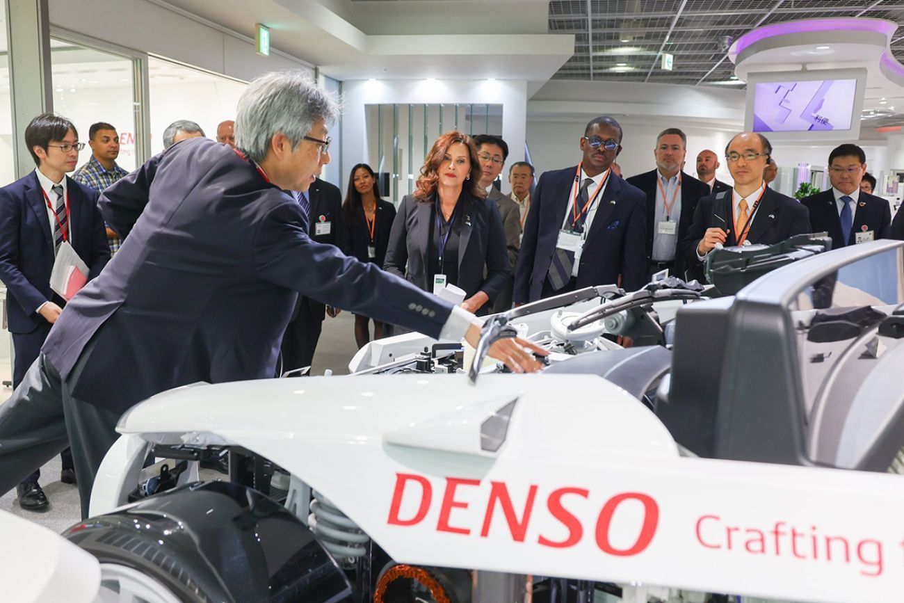 Gov. Gretchen Whitmer looking at a white Denso car. Others are also looking at the car. 