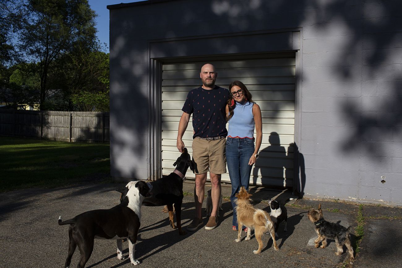 Kim Bode and Josh Byler pose outside. They are surrounded by dogs.