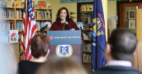 Gov. Gretchen Whitmer at a podium with bookshelves behind her