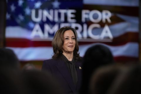 Vice President Kamala Harris stands in front of a screen that says "Unite for America" 