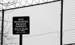 No trespassing sign outside prison fence with barbed wire