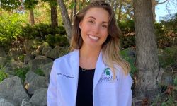 Medical student Sierra Silverwood headshot. She is standing outside and she's wearing a white coat