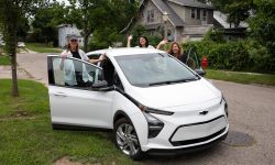 Bridge Michigan journalists Paula Gardner, Kelly House and Asha Lewis pose for a picture around a white EV