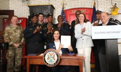 Gov. Gretchen Whitmer holds up the signed budget. She is in a firehouse with people surrounding her, clapping