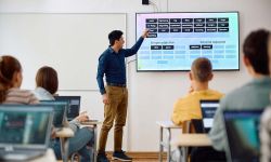 Male teacher using interactive whiteboard while giving a lesson to high school students in the classroom.