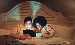 A couple in bed looking at a tablet in an ad for BetRivers