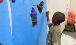 A boy paints on paper hanged on the wall