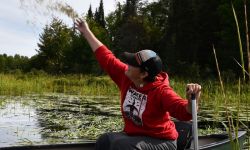 Cortney Collia is sitting in a boat. She is throwing seeds. 