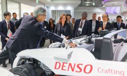 Gov. Gretchen Whitmer looking at a white Denso car. Others are also looking at the car. 