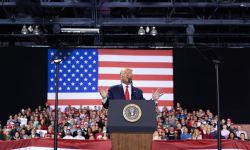 Donald Trump on a stage. People are behind him. 